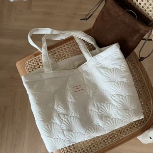 Detailed shell-pattern quilting on a white puffy tote bag placed on a rustic woven chair