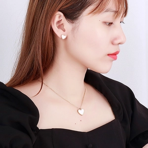 Nahaufnahme eines Models mit herzförmigem Perlmutt-Anhänger und goldenen Ohrsteckern