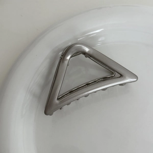 Close-up of minimalist silver metal triangular hair claw clip on white ceramic plate