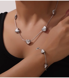 Detail of silver snake chain necklace and bracelet set with heart pendants on a model