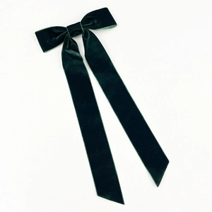Detail of dark green velvet bow hair clip showing elegant long ribbons and fabric texture