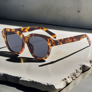 Detail of tortoiseshell square sunglasses with triple metal rivets on stone surface