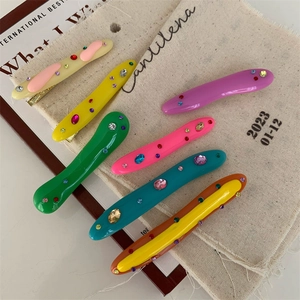 Flat lay of colorful irregular acrylic hair clips with rhinestones on textured fabric