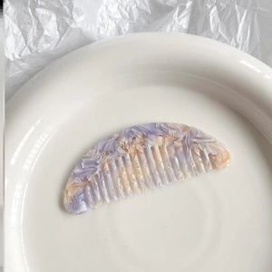 Mini marble pattern acetate hair comb in purple and beige on a white ceramic tray