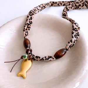 Close-up of a vintage golden fish pendant with leopard print fabric and wooden beads