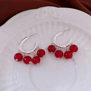 Detailed view of silver C-shaped earrings with three red beads on a ceramic plate
