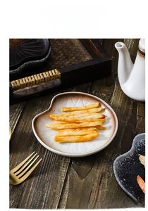 Detail of leaf-shaped ceramic snack plate with brown glazed edge on a wooden table