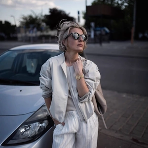Women's cream short flight jacket styled with white striped trousers and sunglasses