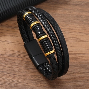 Three-layer braided black leather bracelet with gold metal rings and magnetic clasp on wood