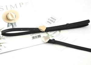 Close-up of two black thin faux leather belts with golden heart buckles on a white background