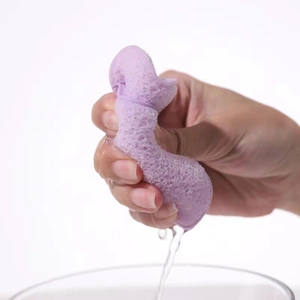 Close-up of hand squeezing water from a porous purple sponge into a glass bowl