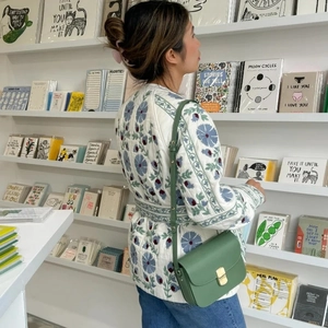 Detail of floral quilted cotton jacket and green leather crossbody bag in a cozy lifestyle setting