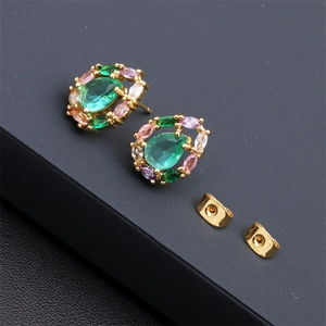 Macro shot of gold-plated teardrop earrings with green and pink zircons on black leather
