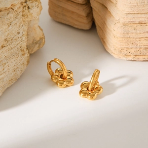 Mirror-polished 18K gold floral hoop earrings on a light-colored natural stone background
