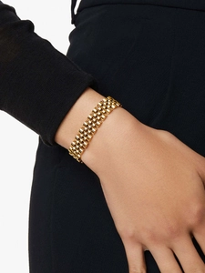 Close-up of a wide gold stainless steel watch-band bracelet on a model wrist with black backdrop