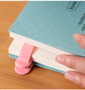 Pink silicone page-tracking bookmark clipped on a blue hardcover book for easy reading