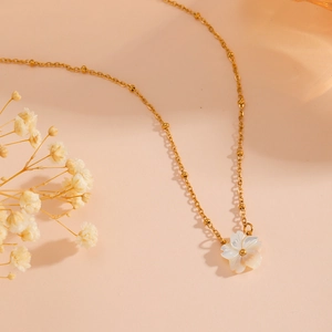 Gold stainless steel necklace with white shell flower pendant on a pink background