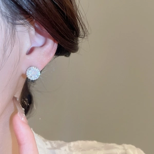 Close-up of sparkling round zircon stud earring on ear with silver finish and halo design