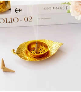 Detailed close-up of golden leaf metal incense burner with burning cone and smoke