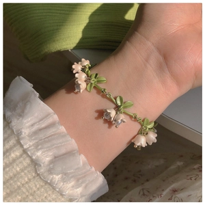Detailed close-up of a pink lily of the valley bracelet on a model wrist with green leaves