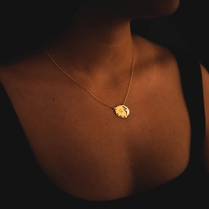 Close-up of golden sun and moon face pendant necklace on model with metallic luster