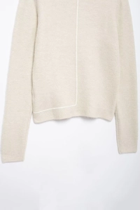 Close-up of beige knit sweater showing unique white exposed stitching and ribbed hem texture