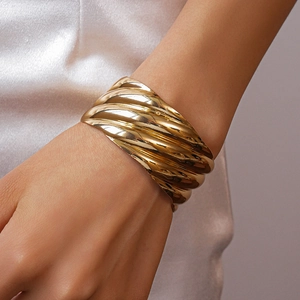 Close-up of gold chunky textured wave bangle on white silk for a luxury minimalist aesthetic