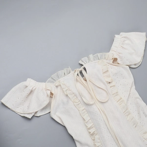 Detailaufnahme des weißen schulterfreien Kleides mit Ösenstickerei und Rüschensaum
