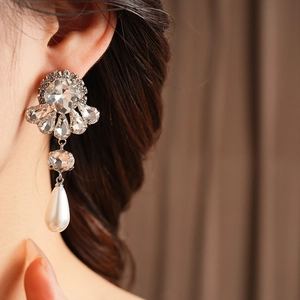 Detailed close-up of a silver flower drop earring with crystals and white pearl on a model
