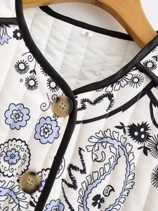 Detail of white quilted jacket featuring blue paisley prints and brown button closure