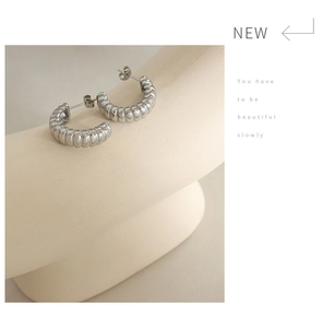 Detail of silver C-shaped hoop earrings with textured thread design on a creative stand