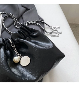 Detail view of black pleated bucket bag with silver chain strap and pearl charm accessory