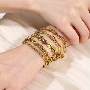 Detailed view of layered 18K gold plated Cuban and clip chains on a textured white fabric
