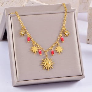 Bracelet doré pendentif soleil avec perles rouges et étoiles sur écrin gris