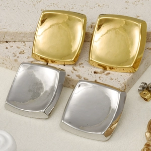 Polished gold and silver square stud earrings displayed on a rustic beige stone surface