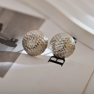 Macro shot of silver metal ball earrings with hammered texture and modern minimalist style