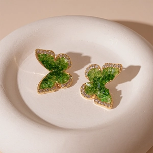 Detail of gold butterfly earrings with green stones and sparkling zircon stones