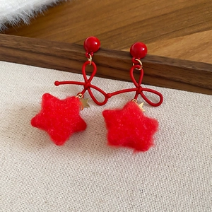 Detail of red bowknot and flocked star drop earrings on a beige fabric background