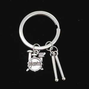Close-up of silver metal drum kit keychain with drumsticks on black background