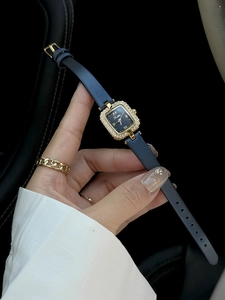 Gros plan d'une montre carrée dorée pour femme avec lunette diamantée et cuir bleu