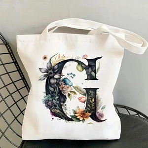 Detailed close-up of a white canvas tote bag with a floral letter G print on a chair