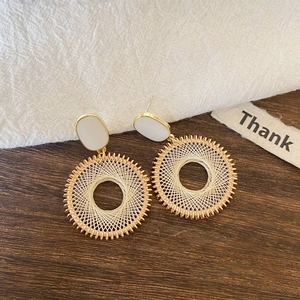 Detail showing bohemian woven mesh earrings with golden trim on a textured fabric
