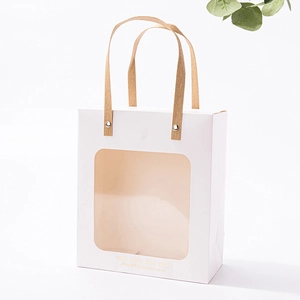 Close-up of elegant white paper gift bag with transparent window and gold text
