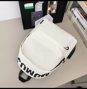 Detail view of white nylon backpack with black printed text on a minimalist desk setup