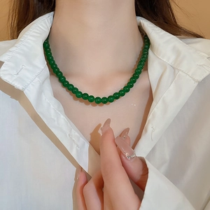 Détail d'un collier en perles de verre vert émeraude porté avec une chemise blanche style minimaliste