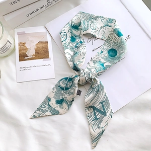 Detail of teal and white silk scarf with letter N pattern on a cozy lifestyle background