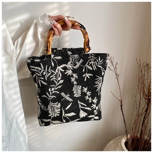 Detail of elegant black cotton linen bag featuring bamboo handles and white floral jacquard