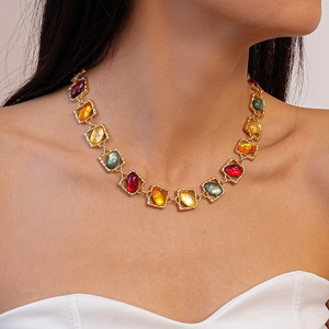Detail of colorful resin gemstones on a gold necklace worn by a model in white