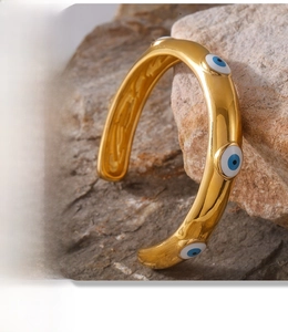 Detail of 18k gold plated stainless steel open bangle with blue evil eye enamel charms
