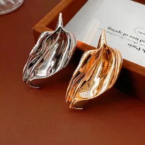 Irregular leaf metal brooches in polished gold and silver on a luxury display